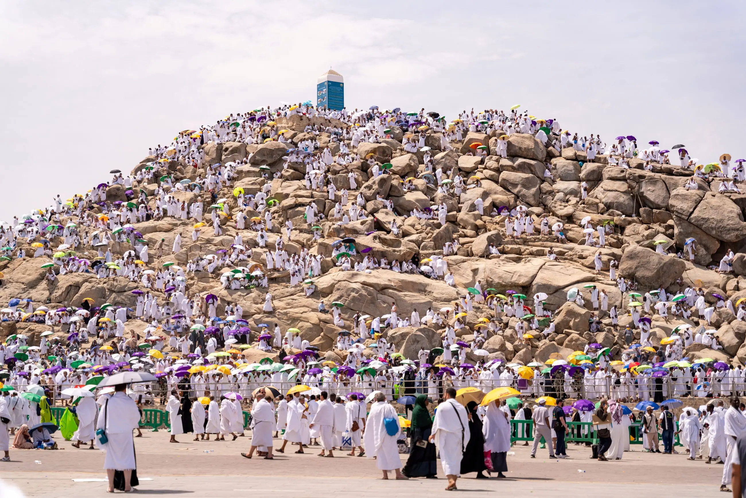 The Mount of Mercy at Arafah covered in pilgrims, the crowd shaded under hundreds of green, purple and yellow umbrellas in the midday heat.