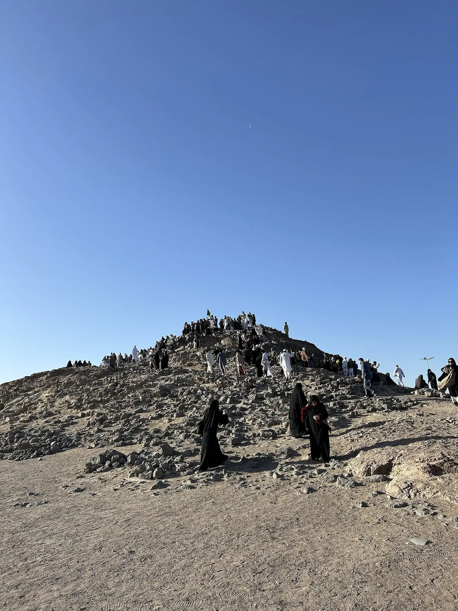 Archers’ Hill at Uhud, a low rise of dark broken stone under a clear sky, with a few visitors standing at the summit.